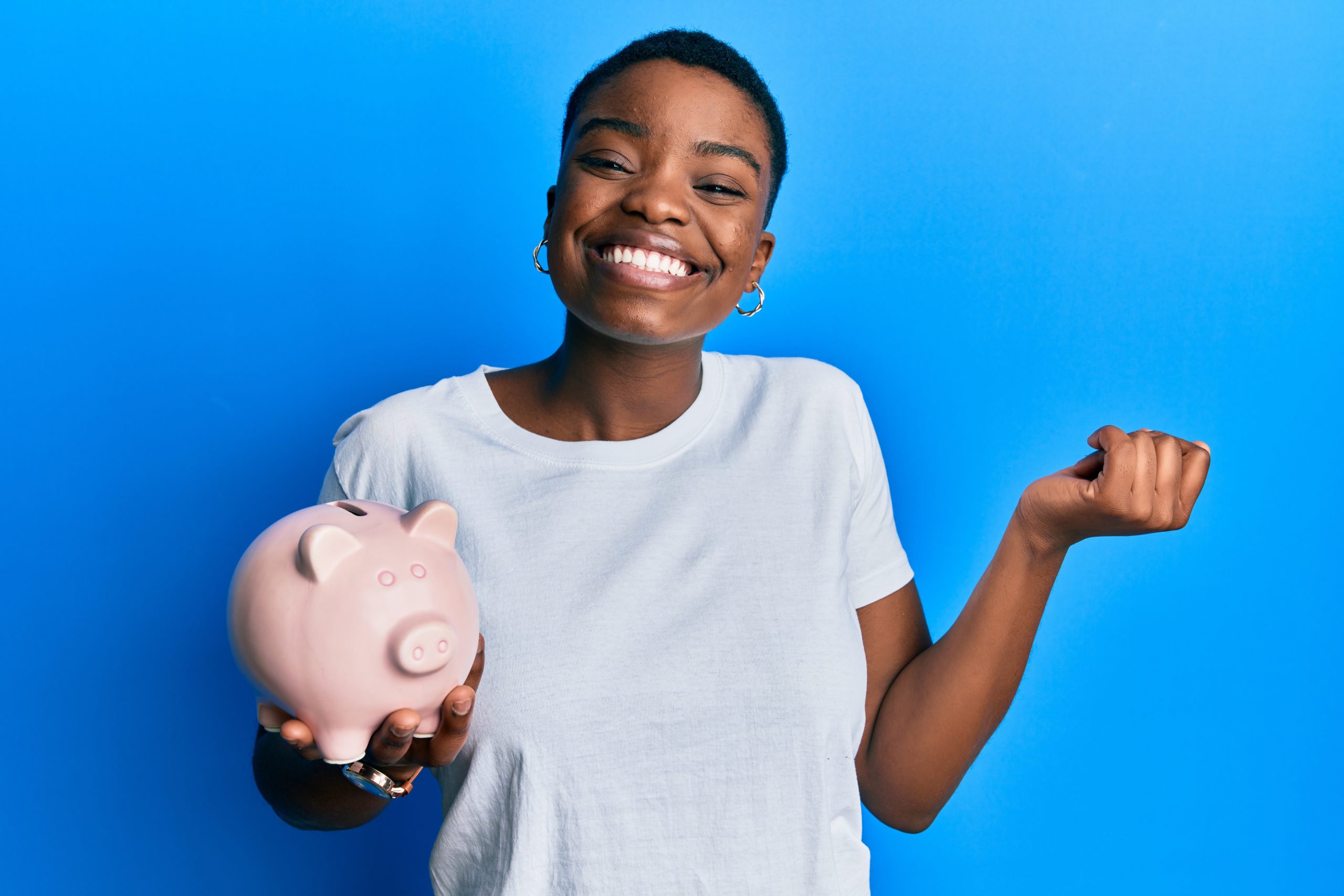Young african american woman holding piggy bank screaming proud, celebrating victory and success very excited with raised arm